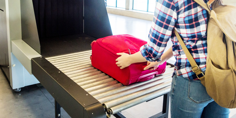 En resenär lägger en resväska på ett rullband vid säkerhetskontrollen.